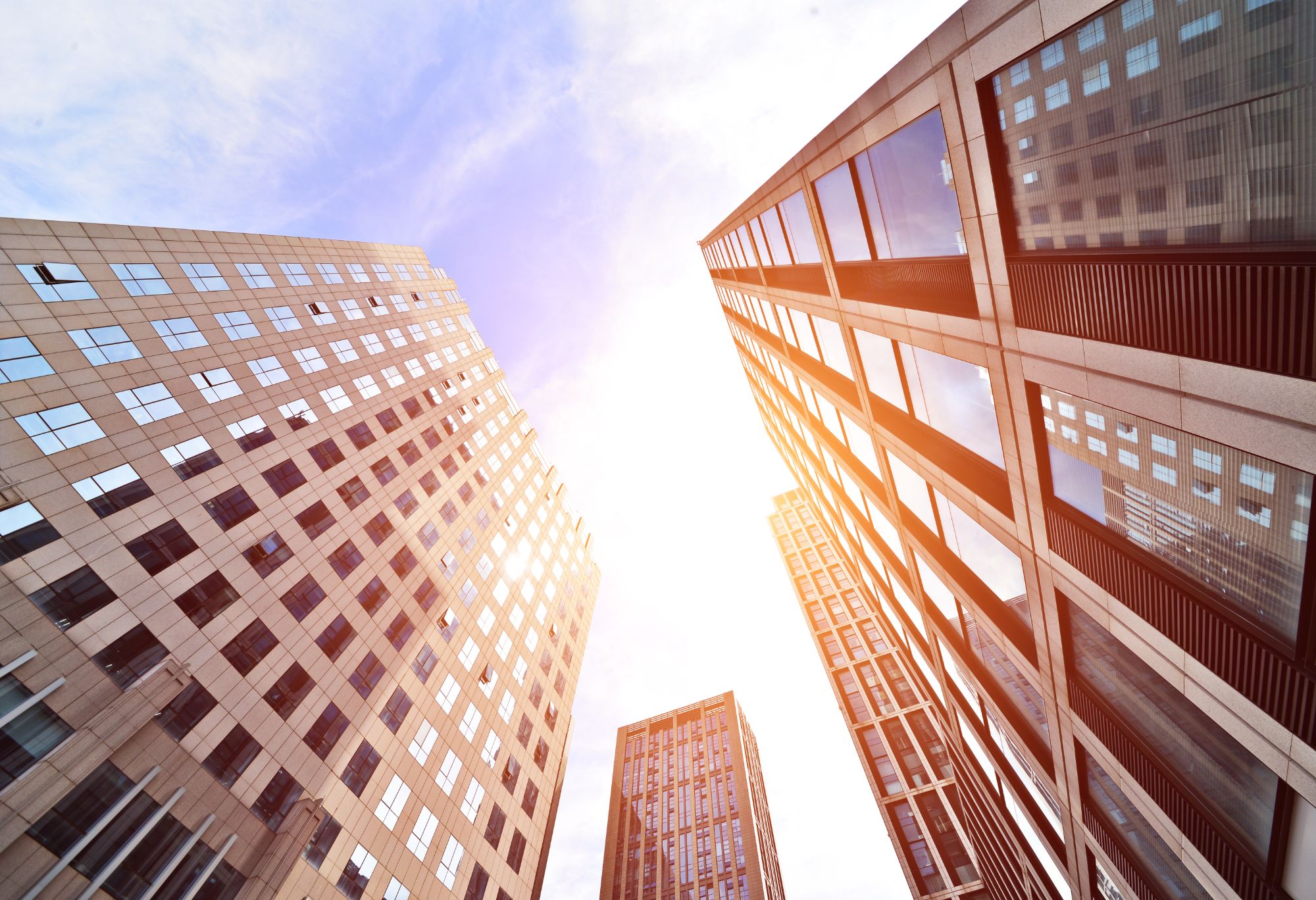 Edifícios residenciais e comerciais vistos de baixo, com o céu e o sol ao fundo